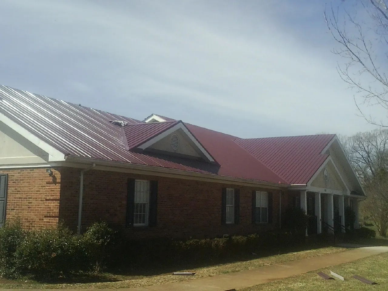 Red metal roof with gabled entries on a long brick building, from a Hail Damage Roof Repair job in Atoka