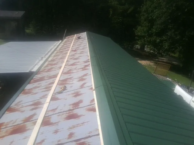 Old rusted panels beside newly installed green metal roofing — Wind Damage Roof Repair by Roofing Brothers in Atoka