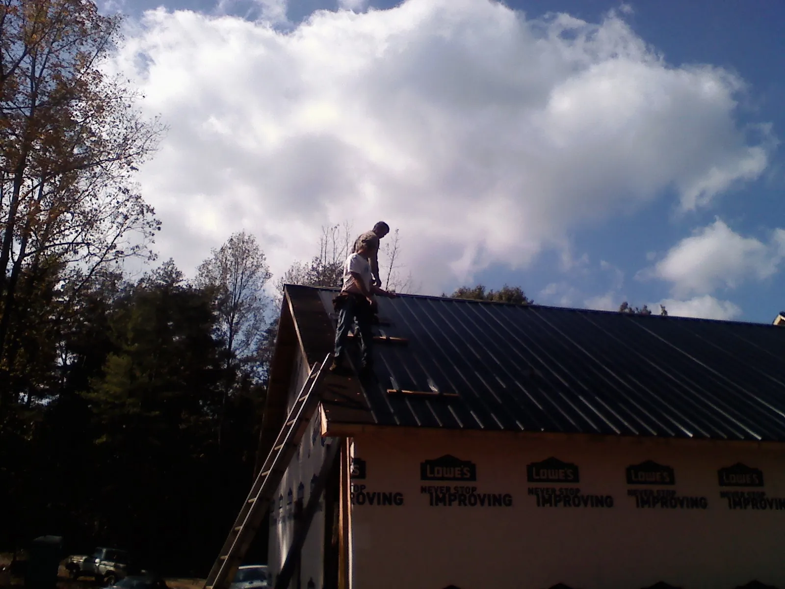 Roofer fastening dark metal panels high against a cloudy sky, from a Roof Inspection job in Atoka