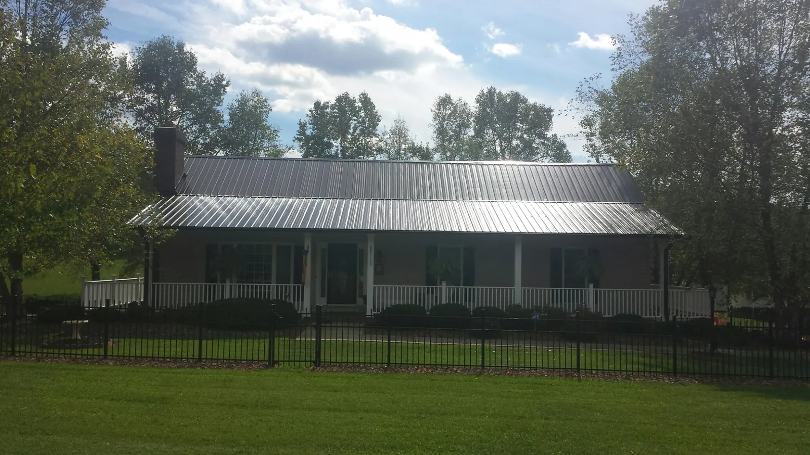 Gray metal roof on a brick ranch with a full width front porch — Gutter Guard Installation work by our crew in Atoka