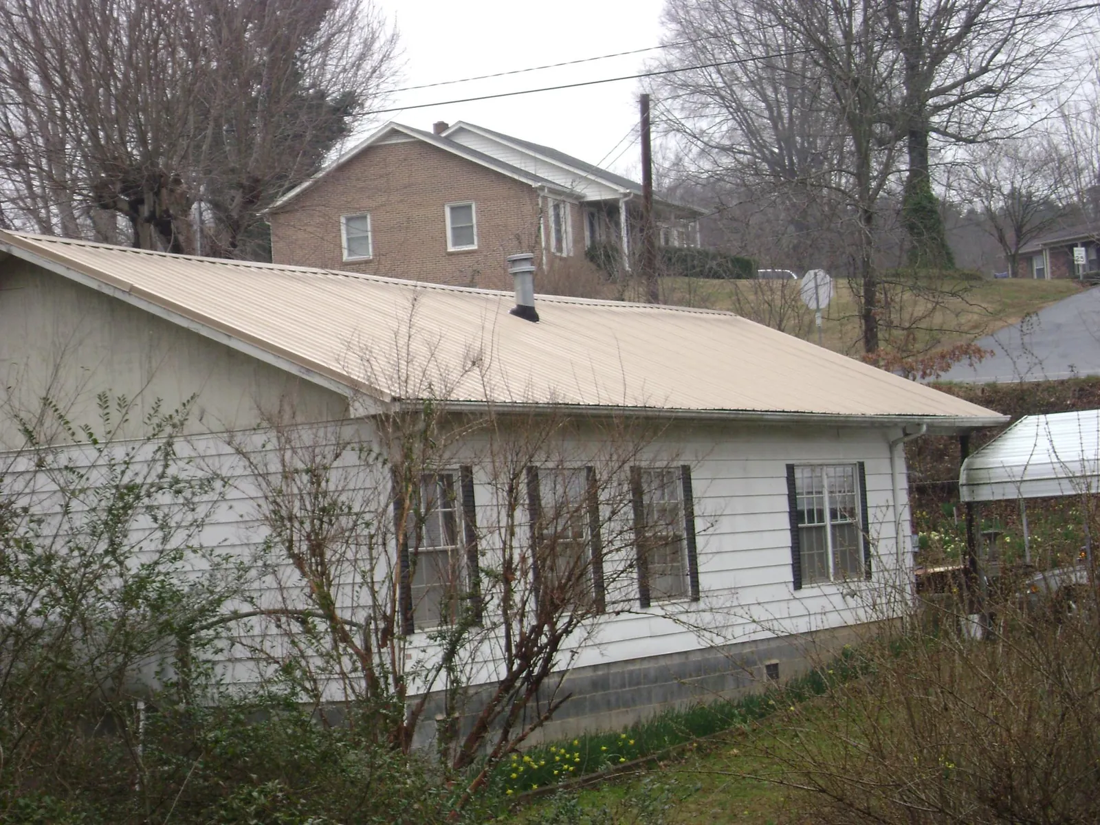 Tan metal roof on a white sided house set into a hillside — Commercial Roofing by Roofing Brothers in Atoka