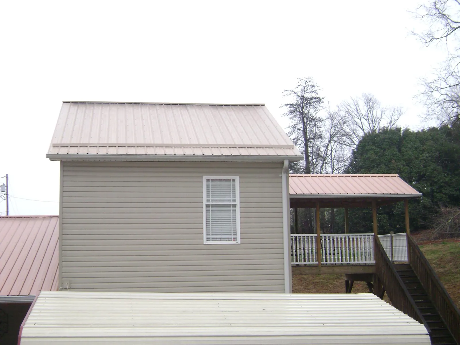 Tan metal roofs on a two story addition and attached porch, from a Roof Replacement job in Atoka